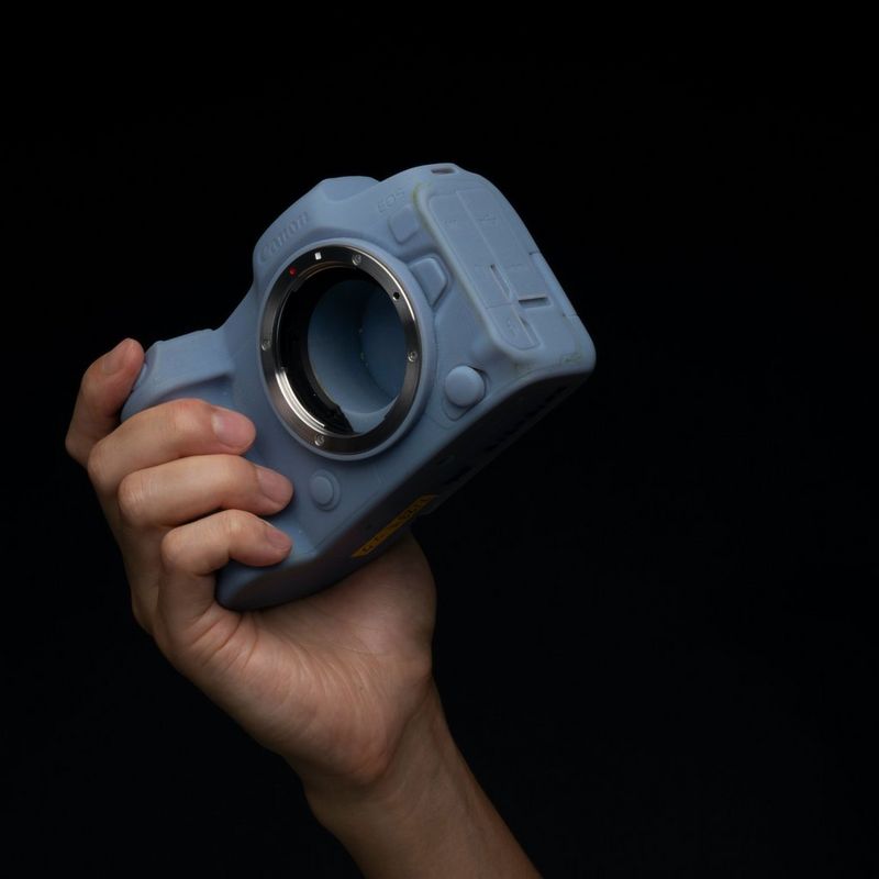 Een hand houdt een model van een Canon EOS R5-camera omhoog.