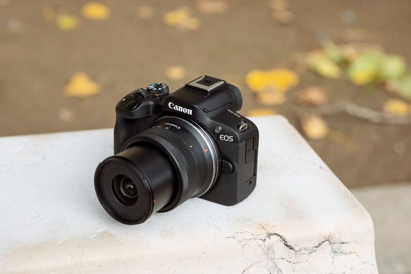 A Canon EOS R50 camera with its kit lens extended positioned on a white surface.