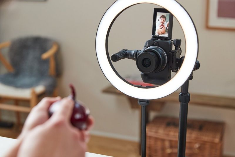 A Canon EOS R50 set up vertically on a tripod with a ring light and microphone. The vari-angle touchscreen shows food influencer Martyn Odell holding a red onion.