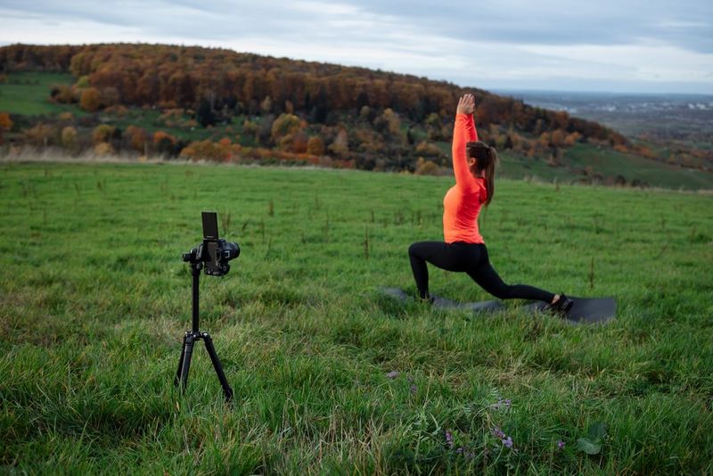 Canon EOS R50 su un treppiede che riprende la content creator Elena Bulkowski in top arancione che esegue una posizione yoga in un campo.