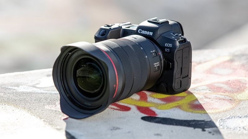 A Canon EOS R5 camera sits on a graffitied piece of concrete.