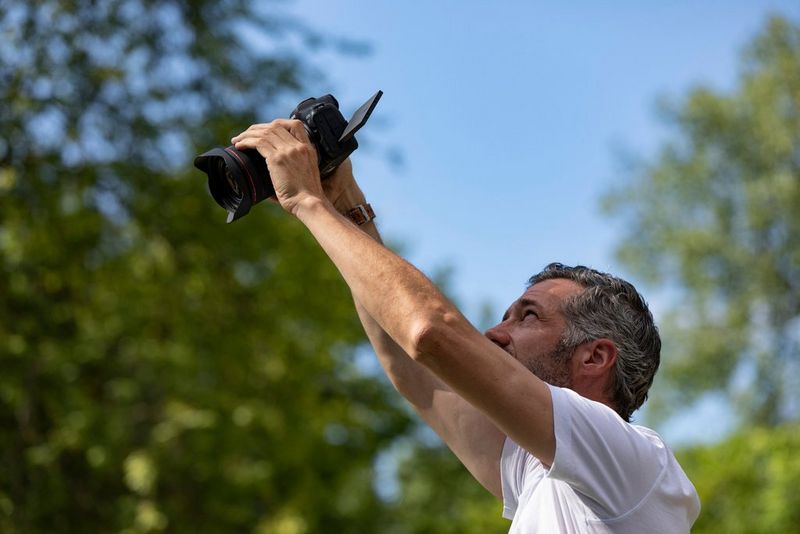 A photographer holding a Canon EOS R5 high above his head, looking at its vari-angle screen.