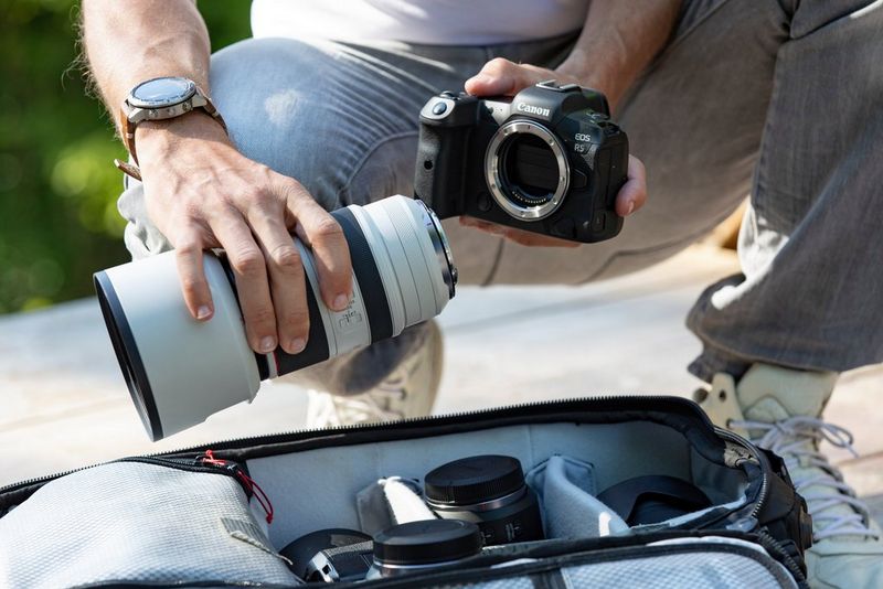 Een man heeft een Canon EOS R5 in zijn ene hand en een Canon-teleobjectief in de andere hand, boven een uitrusting met andere objectieven.