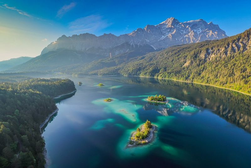Een luchtfoto van een licht landschap met kalm water bezaaid met eilanden en omgeven door boomrijke heuvels.