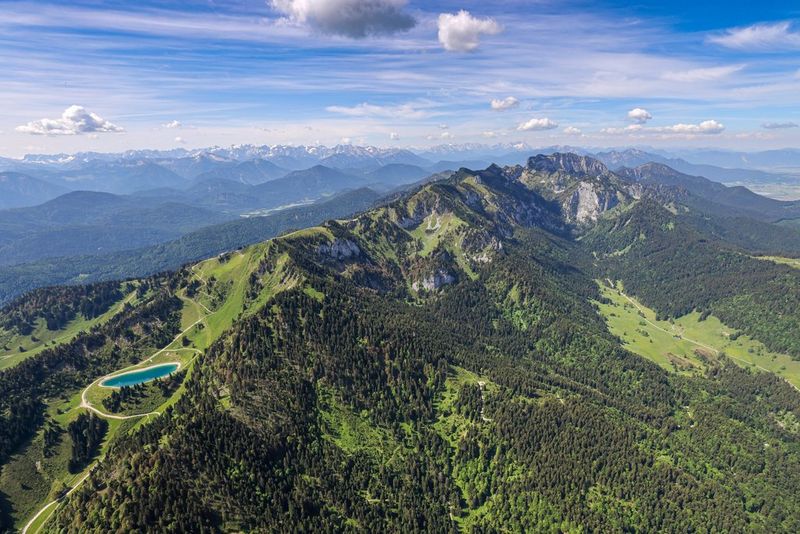 An aerial view of a ridge of verdant mountains, with a distant mountain range in the background and fluffy clouds in the sky, photographed by adventure travel photographer Ulla Lohmann on a Canon EOS R5.