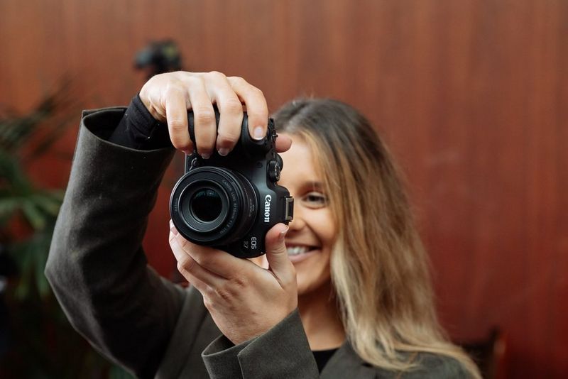 Creative portrait photographer Rosie Hardy smiles as she holds up a Canon EOS R7 and looks at its rear screen.