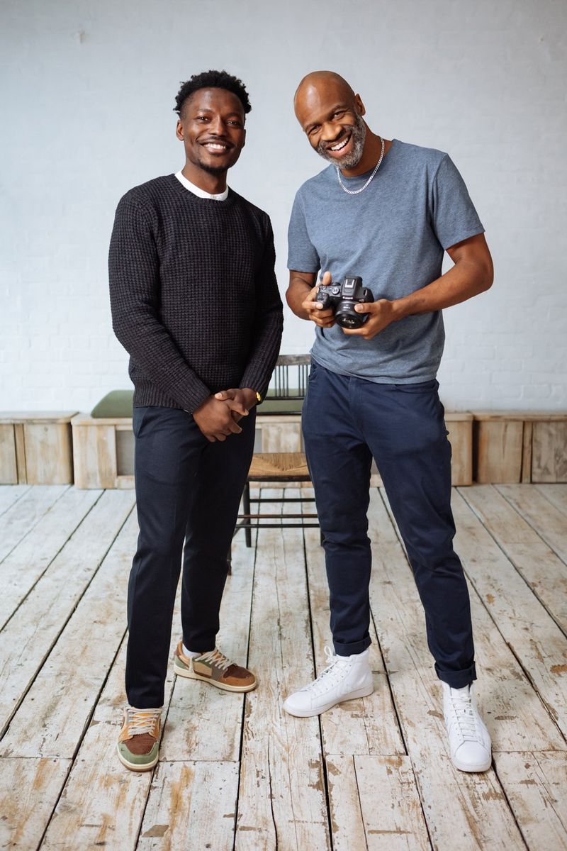 Tomi Adebayo et Kid Circus se tiennent côte à côte en souriant et Kid tient un appareil photo Canon.