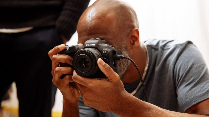Photographer Kid Circus looks through the viewfinder of a Canon EOS R5 camera.