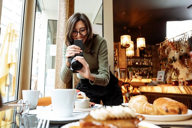 Laura Hannoun sorridente mentre fotografa caffè e croissant in un caffè di Parigi.