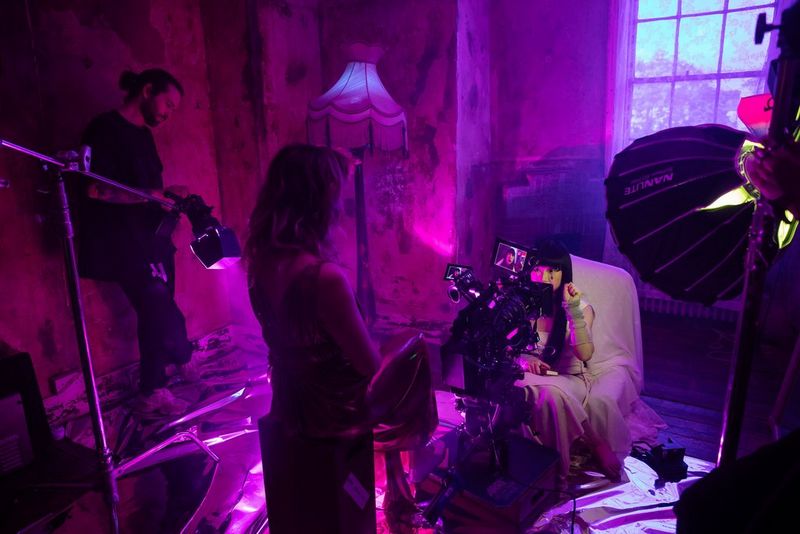 La filmmaker Diana Olifirova in piedi sopra una telecamera cinematografica Canon, mentre registra un primo piano del viso di una persona.