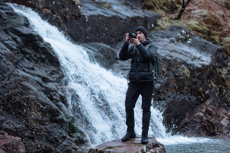 Il videografo e fotografo Harrison Brown regge una fotocamera Canon; alle sue spalle una cascata scorre tra le rocce.