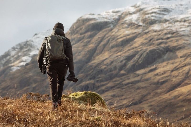 Mentre le montagne si stagliano all'orizzonte, Harrison Brown, zaino in spalla e macchina fotografica tra le mani, si allontana dalla fotocamera.
