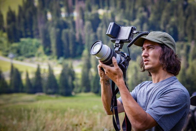 Le photographe sportif Teddy Morellec se tient devant des montagnes boisées et filme avec un Canon EOS R6 Mark II.