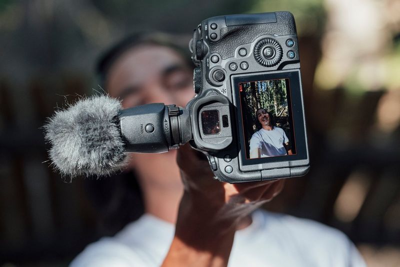 Un fotografo che si riprende utilizzando Canon EOS R6 Mark II e un microfono esterno collegato, mentre l'immagine viene visualizzata sullo schermo posteriore della fotocamera.