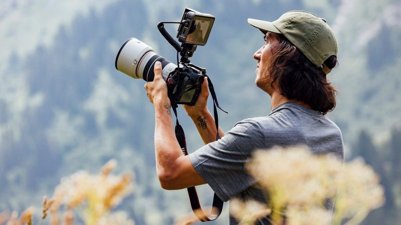 Teddy Morellec shooting video in a field using a Canon EOS R6 Mark II with a monitor mounted on its hotshoe.