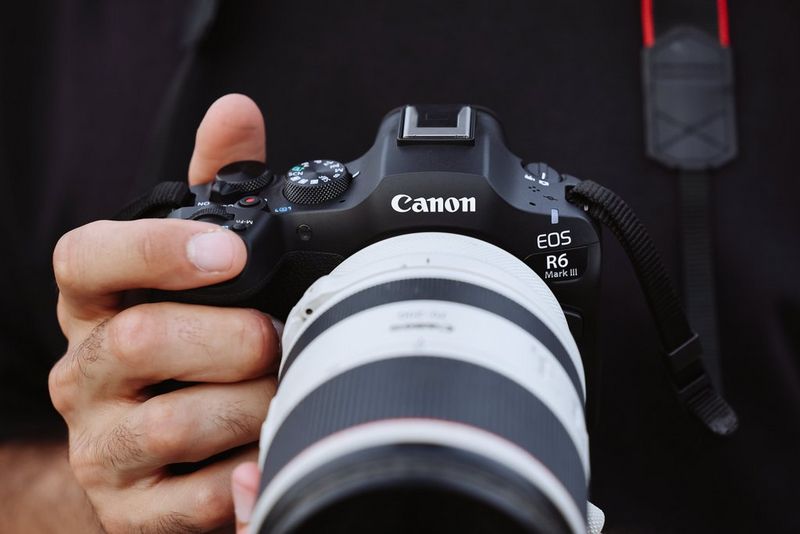 Un primo piano mostra le mani di un fotografo che impugna Canon EOS R6 Mark III con un obiettivo RF serie L.