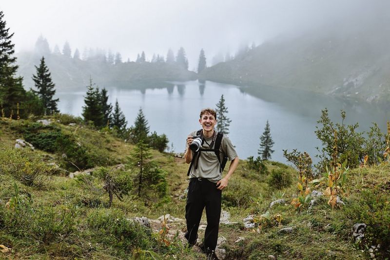 Photographer Leo Thomas stands holding a Canon EOS R6 Mark III in front of a serene, misty lake scene in southern Germany.