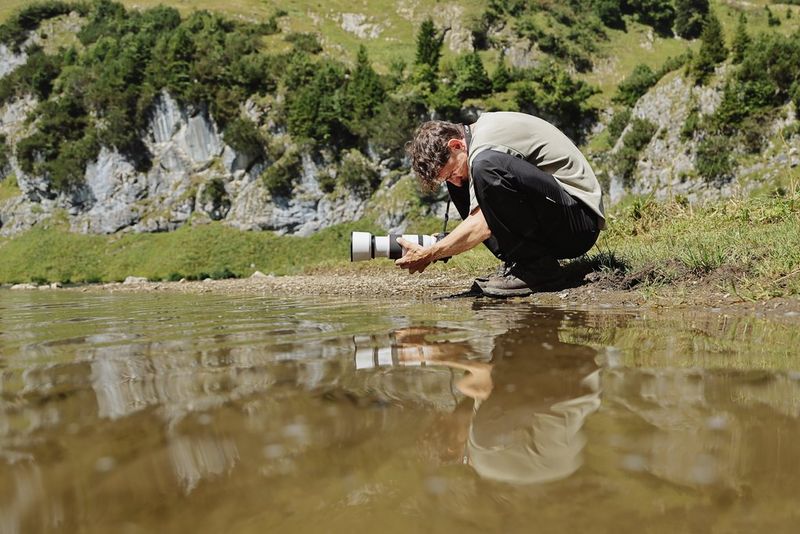 Leo Thomas hält eine Canon EOS R6 Mark III nah an die Oberfläche eines Sees und sieht dabei auf das dreh- und schwenkbare Display der Kamera.