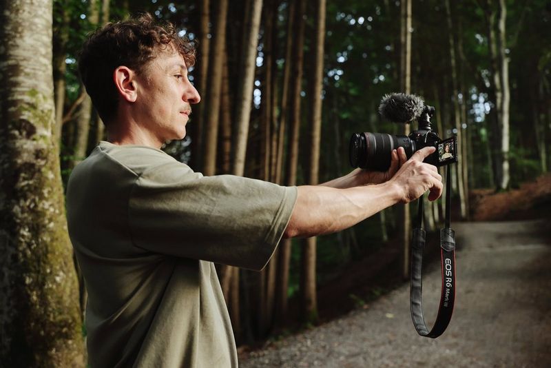 Photographer and content creator Leo Thomas in a forest, pointing the Canon EOS R6 Mark III towards himself and operating the camera via the vari-angle screen that's folded out and facing him.