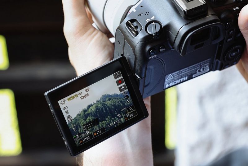 A person holds the Canon EOS R6 Mark III, with the Vari-angle touchscreen showing a rural scene being filmed.