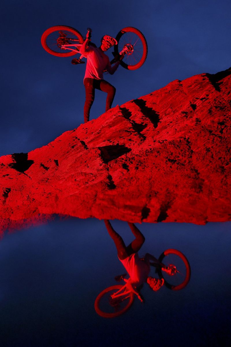A cyclist, bathed in dramatic red light, carries his bike on his shoulders while walking carefully over rocky terrain. Taken on a Canon EOS R6 Mark III. 