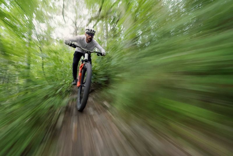 A mountain biker speeding towards the camera, in sharp focus with the surrounding forest greenery blurred. Action photo by Jean-baptiste Liautard taken on a Canon EOS R6 Mark III with a Canon RF 10-20mm F4L IS STM lens.