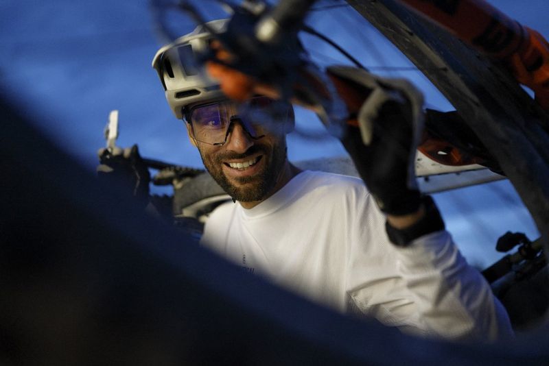 A cyclist smiles at the camera through the wheels of a bike that he is holding across his shoulders. Taken on a Canon EOS R6 Mark III. 