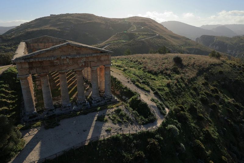 Un temple au sommet d'une colline projette de longues ombres sur le sol tandis que le soleil se couche derrière lui.
