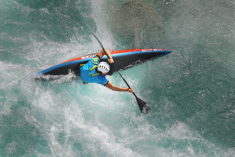 O persoană într-un caiac albastru, pe creasta unui val.