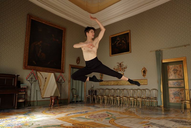 Ballet dancer Lee Jay Hoy captured in mid-air as he leaps across an ornately decorated room.