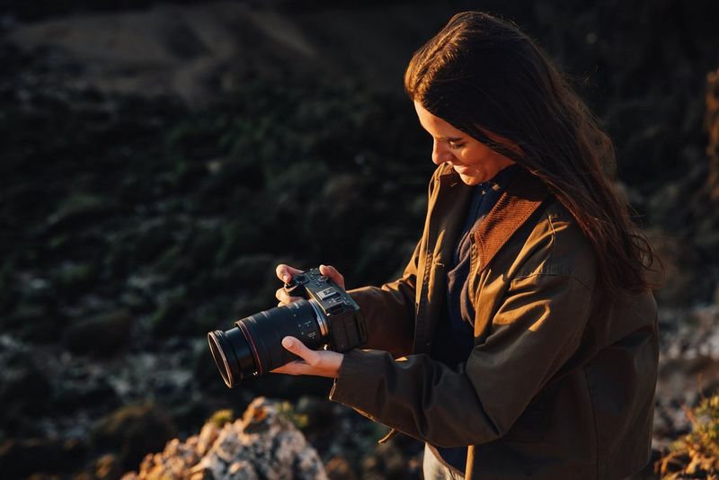 Filmmaker Giulia Gartner, lit by warm light and holding a Canon EOS R6 V against a dark landscape.