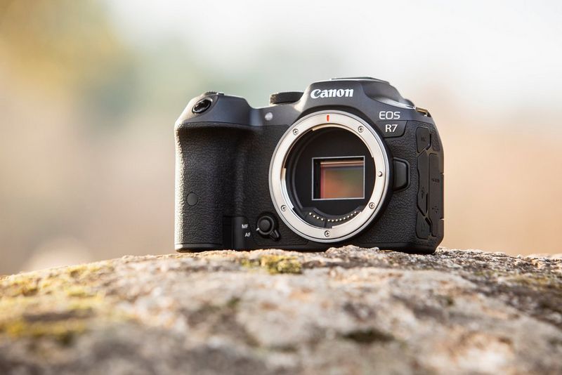 A Canon EOS R7 camera with no lens attached on a rocky surface.