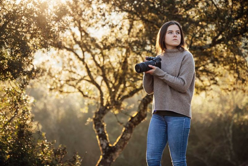 A person in a woodland setting holding a Canon EOS R7 and looking to one side.