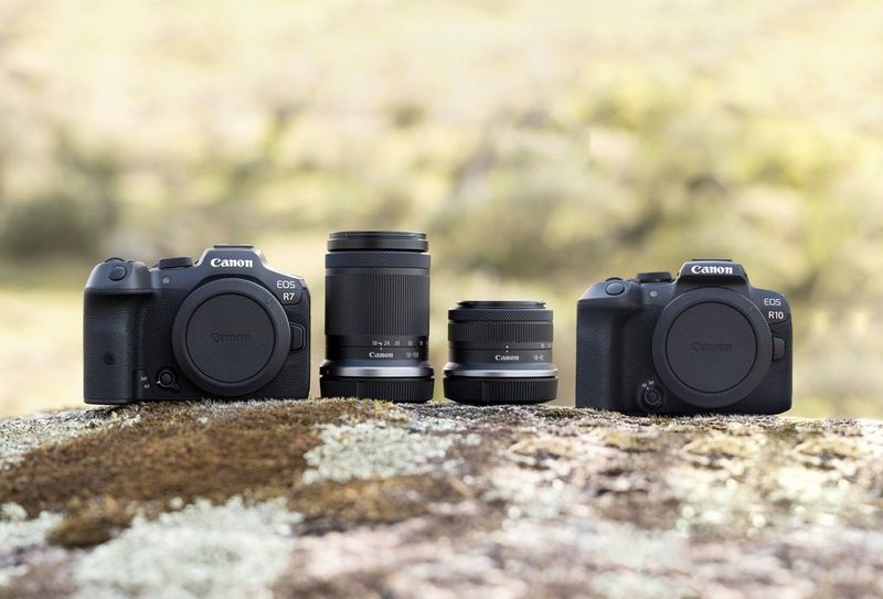 The Canon EOS R7 and Canon EOS R10, with two Canon lenses between them, on a large rock.