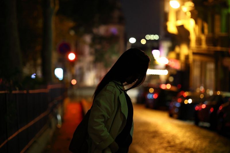 A woman crosses a road at night, with cars and traffic signals blurred in the background, taken on a Canon EOS R8 with a Canon RF 85mm F2 MACRO IS STM lens.