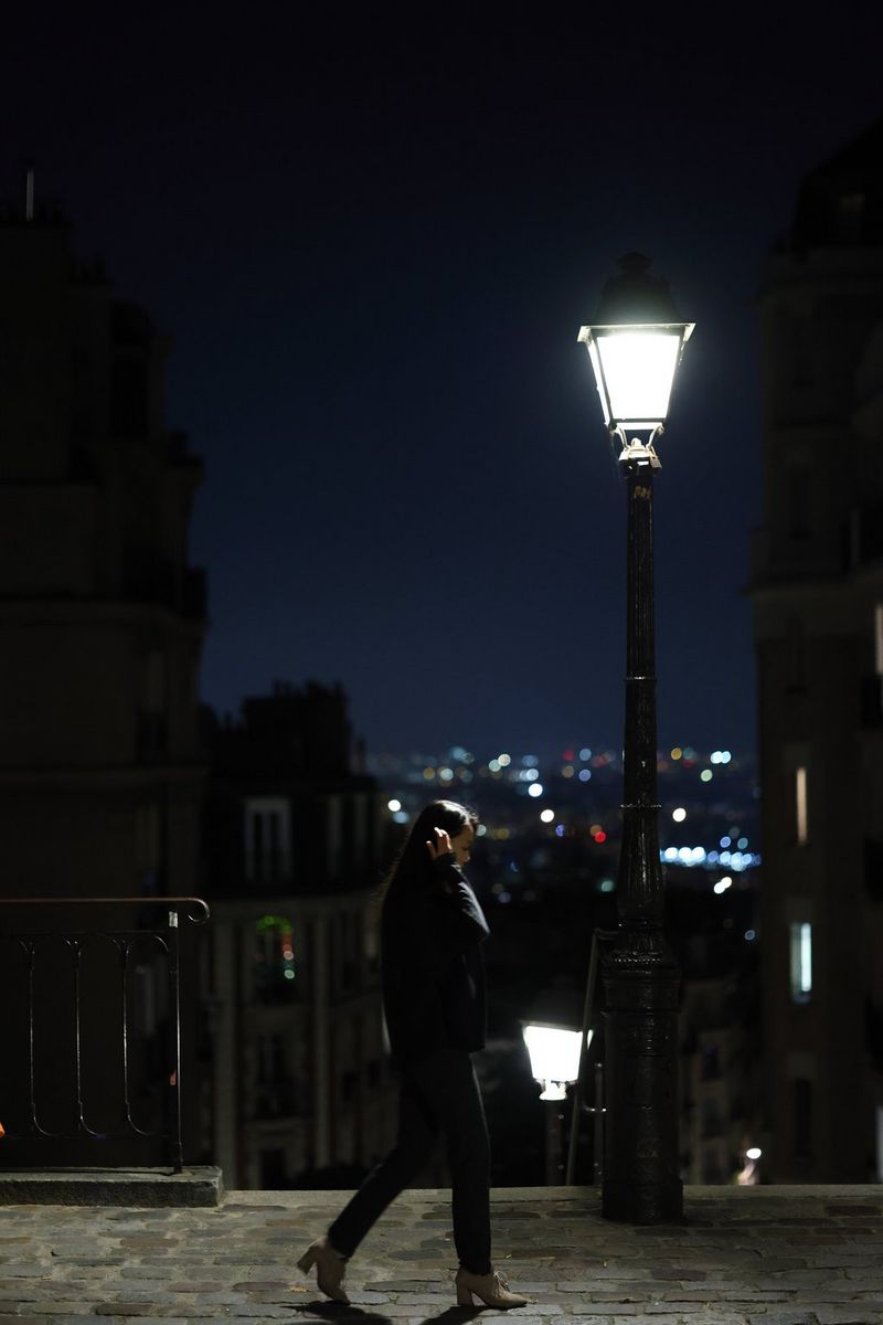 A picture taken on a Canon EOS R8 of a woman crossing the road at night, with the distant lights of the city visible in the background. 