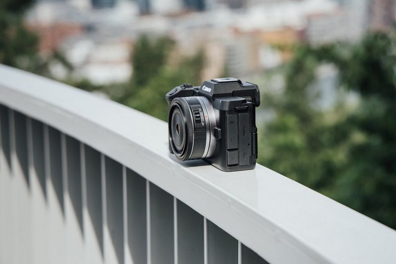 A Canon EOS R8 Mark II sits on a handrail in front of a city. The camera in the foreground is in sharp focus while the background is blurred.