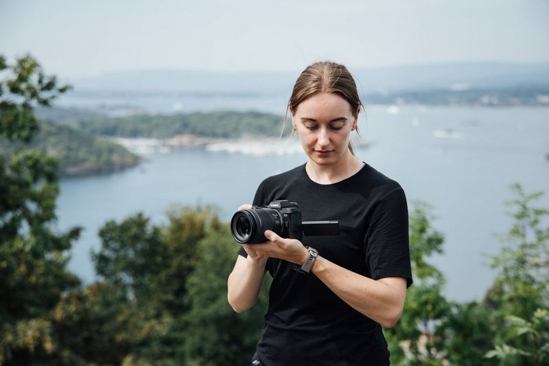 Photographer Frauke Hameister supports the Canon EOS R8 MARK II as she looks at the vari-angle screen in front of a scenic view.