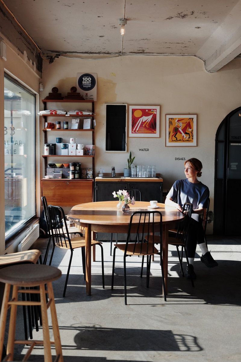 Une femme est assise à une table dans un petit café, le regard tourné vers la fenêtre qui est la seule source de lumière de la pièce. Photo de voyage prise par Frauke Hameister avec un Canon EOS R8 Mark II équipé d'un objectif Canon RF 45mm F1.2 STM.