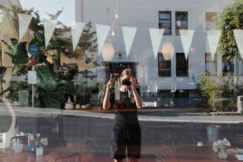 A self-portrait of German photographer Frauke Hameister reflected in a café window, taken using a Canon EOS R8 MARK II camera.