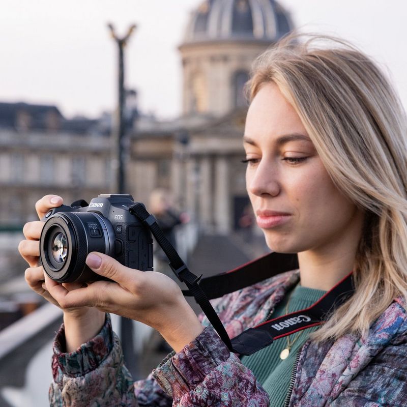 Alexandra Andreeva stands holding a Canon EOS R8, with a large building behind her out-of-focus.