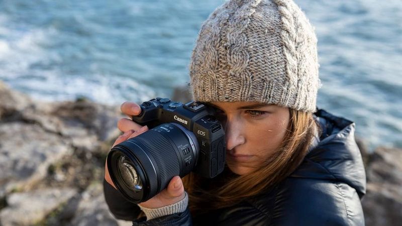 Женщина в шерстяной шапке смотрит в видоискатель камеры Canon EOS RP.