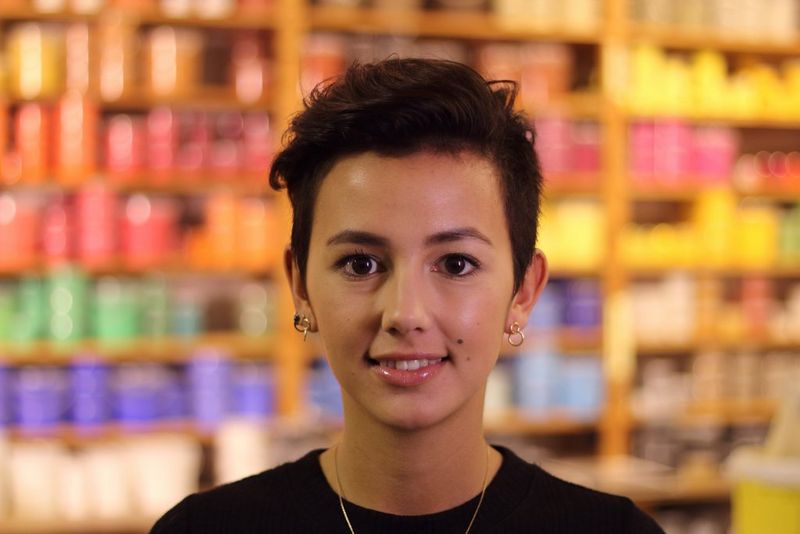 A portrait of a young woman with relatively indistinct coloured shapes in the background.