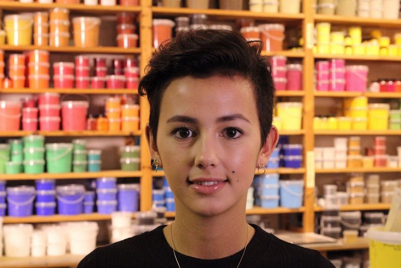 A portrait of a young woman with the background of colourful items becoming quite distinct, if not in perfect focus.