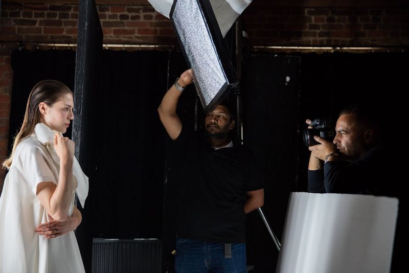 A side profile of a man holding a Canon EOS 5D Mark IV photographing a model in a white dress.