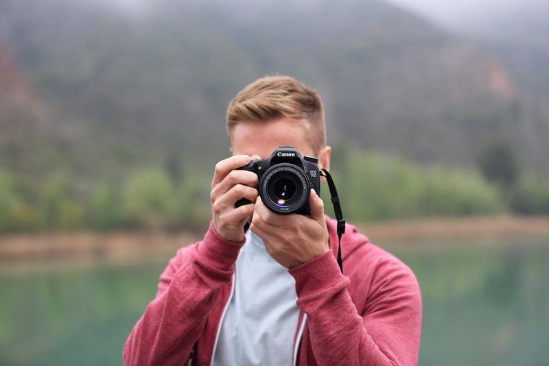 Muž drží fotoaparát pravou rukou a hledáček blízko obličeje a levou rukou podpírá zespodu objektiv.