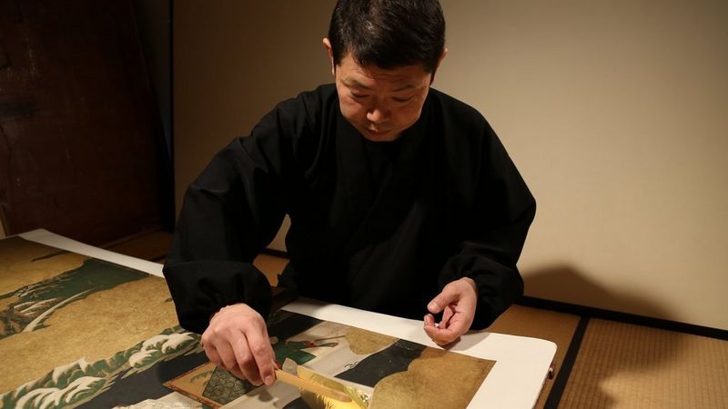 An artisan carefully applying gold leaf to a reproduction of a Japanese screen.