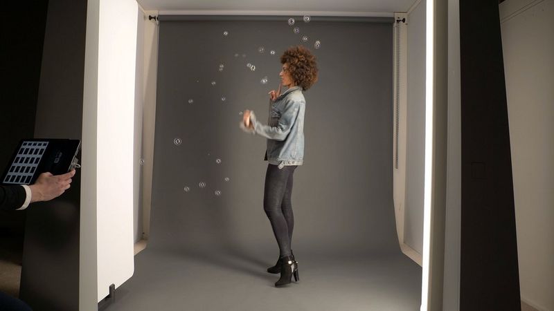 Une mannequin aux cheveux ondulés dans une machine de photographie StyleShoots entourée de bulles.