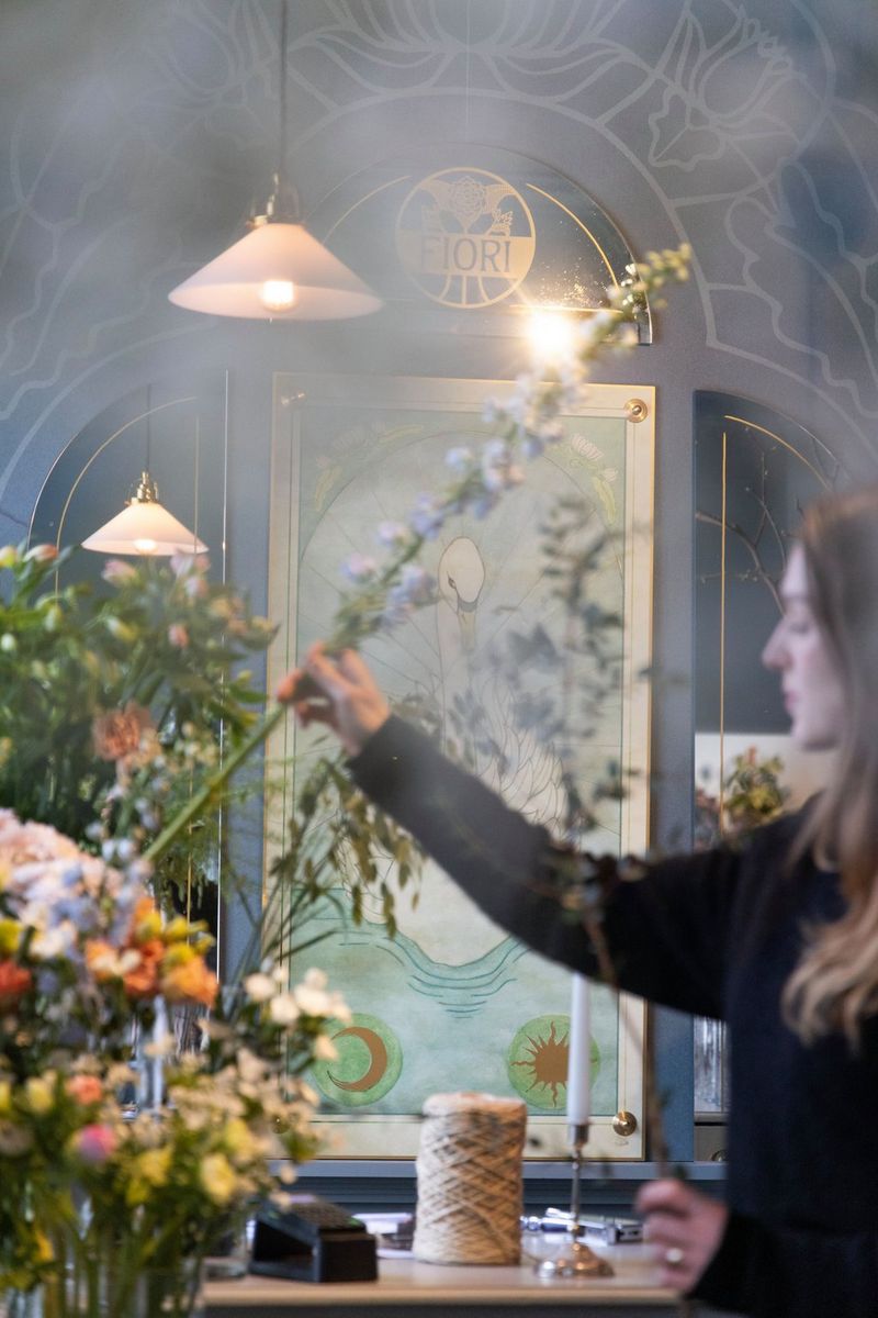 Dame som holder opp blomster. Det henger et speil bak henne med en svane på.