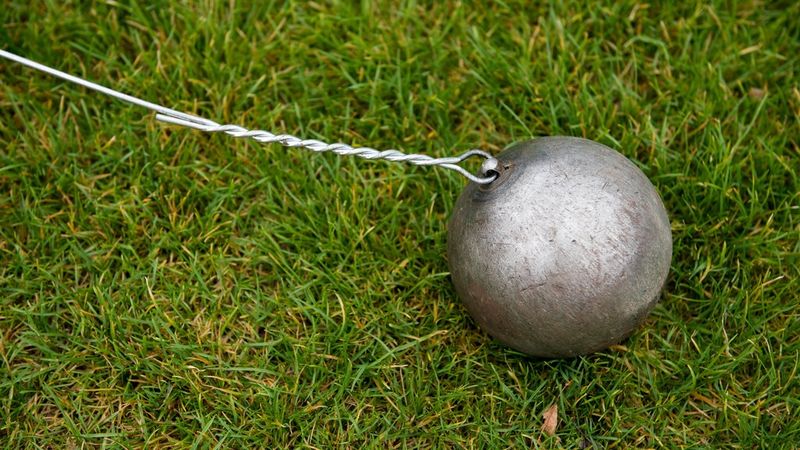 Een zilverkleurige hamerslingerbal, vastgemaakt aan een draad, ligt op het groene gras.